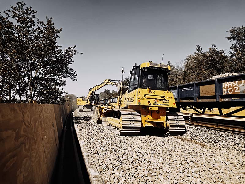 Bulldozer en spoorkraan van Van Eerd verwerken nieuwe ballast naast een werktrein op de metrolijn in Amsterdam